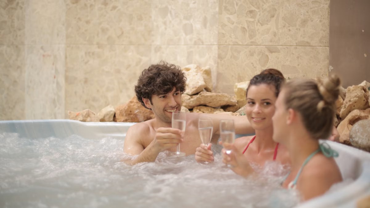 Group of friends toasting with drinks in a hot tub, enjoying relaxation and togetherness indoors.